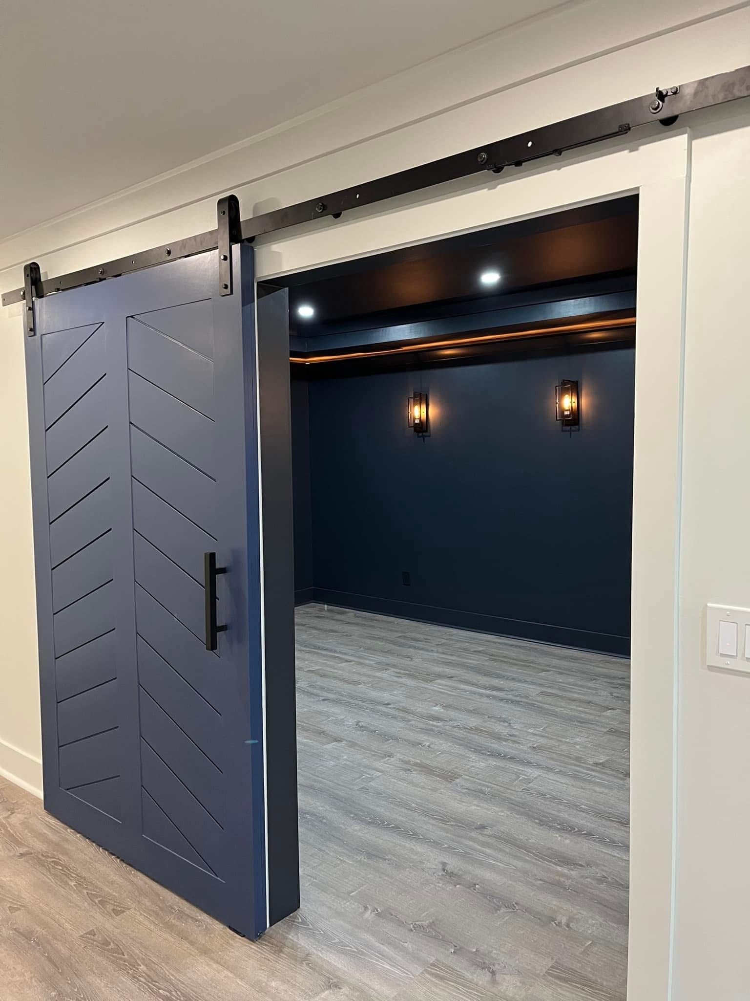 Blue chevron barn door open to a dark blue room with sconce lights and a recessed ceiling.