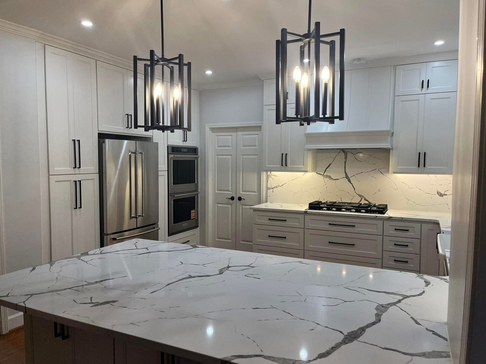 Modern kitchen with white cabinets, large island with marble countertops, and two black pendant lights.