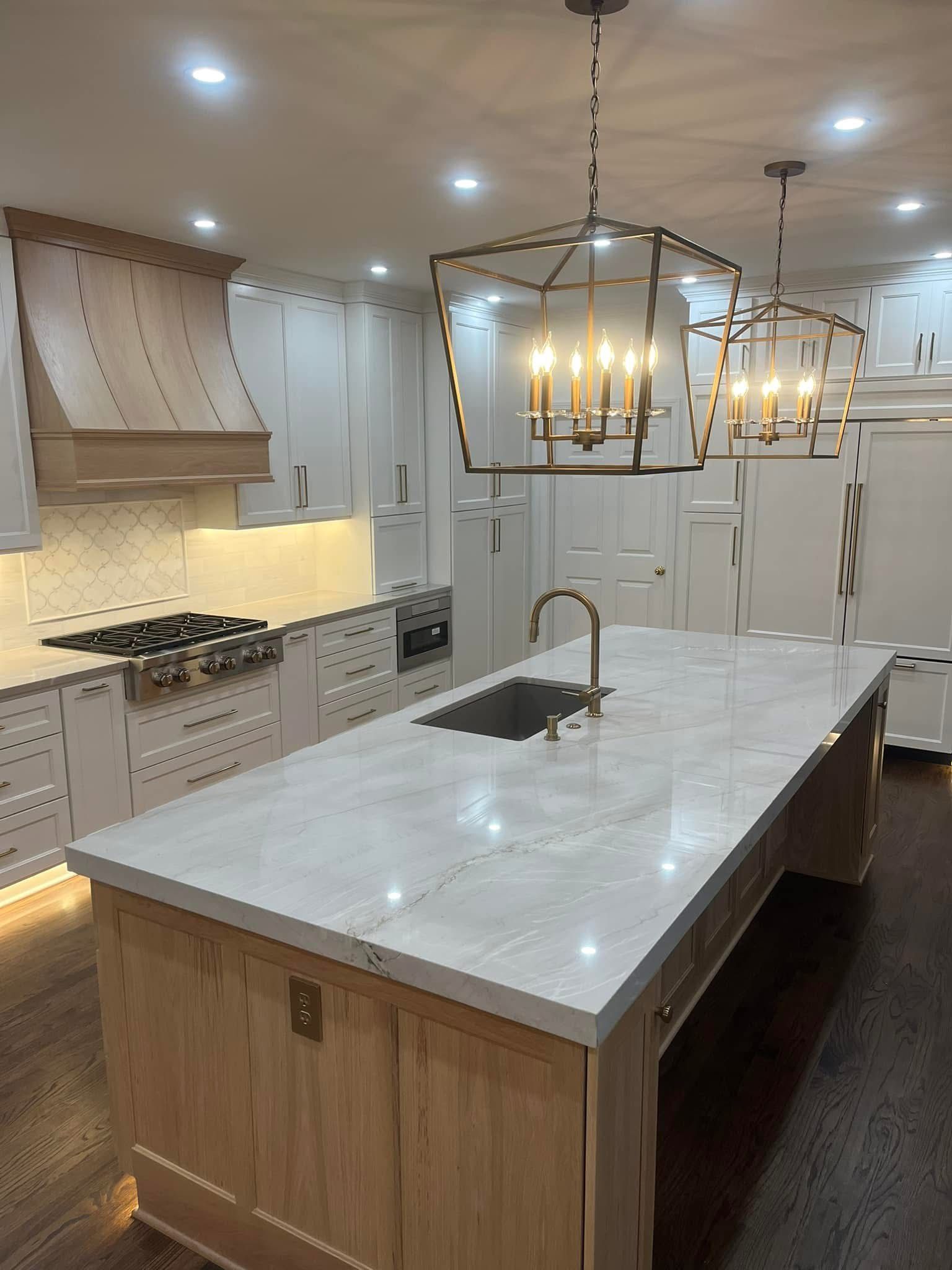 Modern kitchen with white cabinets, light wood island, gold pendant lights, and marble countertops.