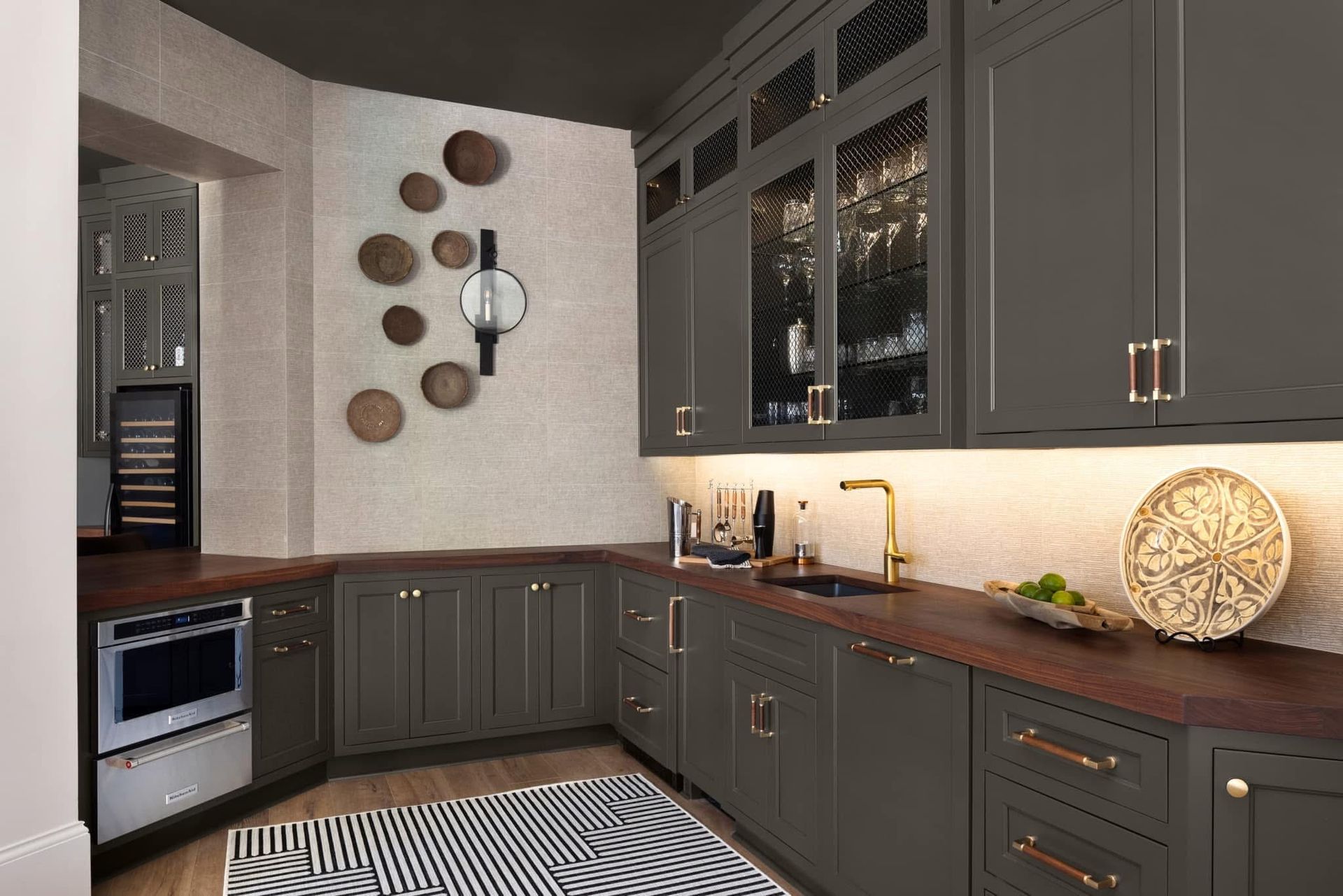 Dark gray kitchen with wooden countertops, gold hardware, and decorative wall art.