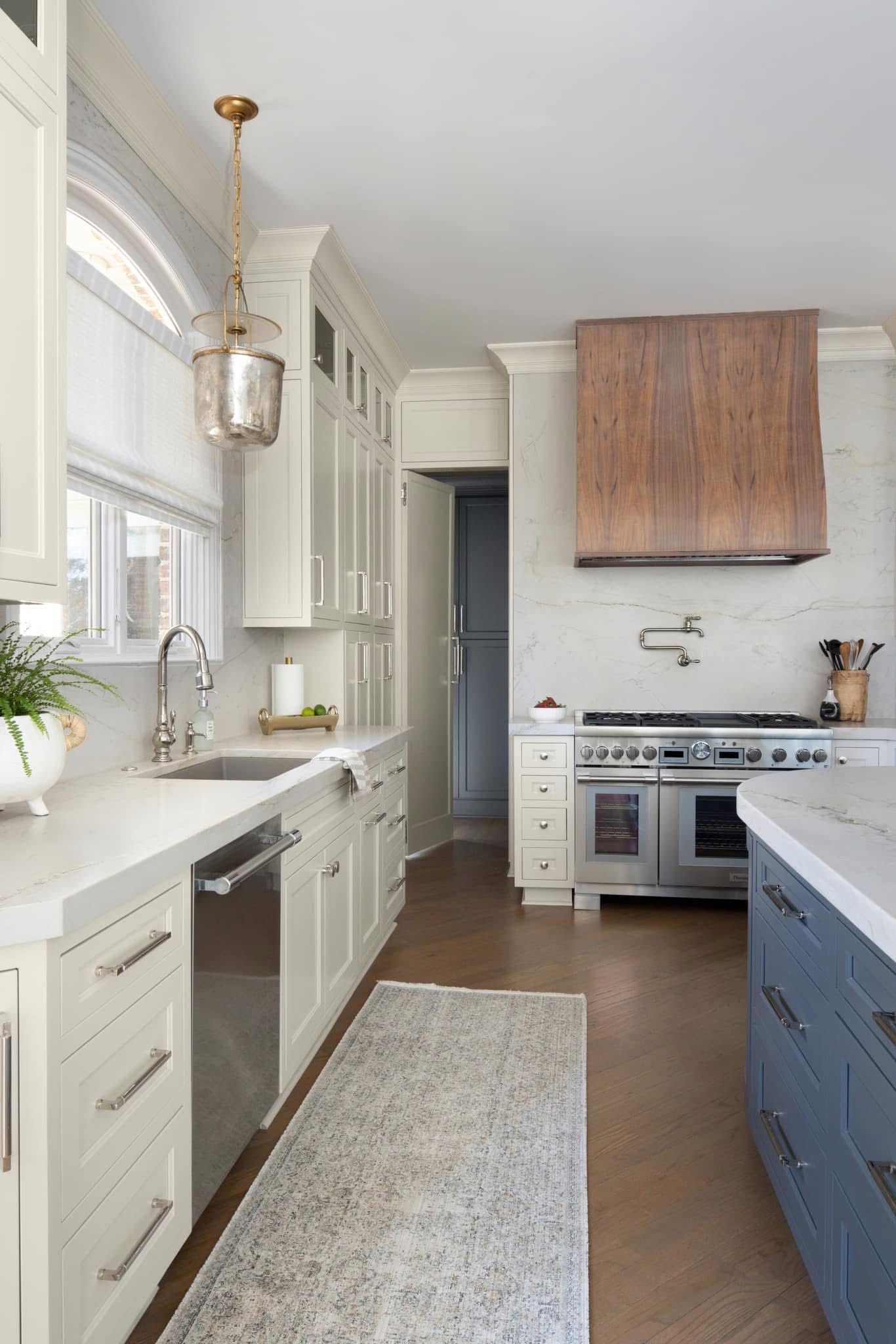 Elegant kitchen with white cabinets, stainless steel appliances, marble backsplash, and wooden range hood.