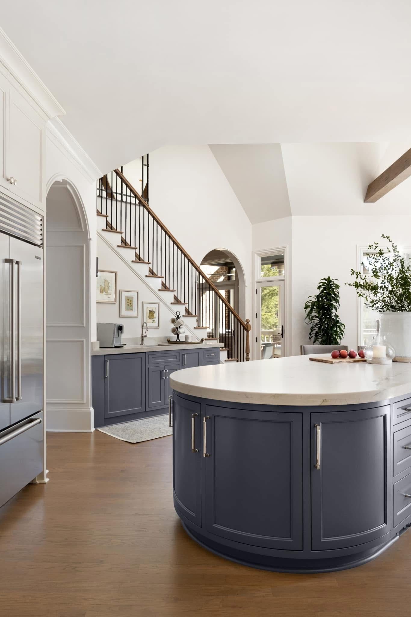 Elegant kitchen with dark blue cabinetry, curved island, and staircase.