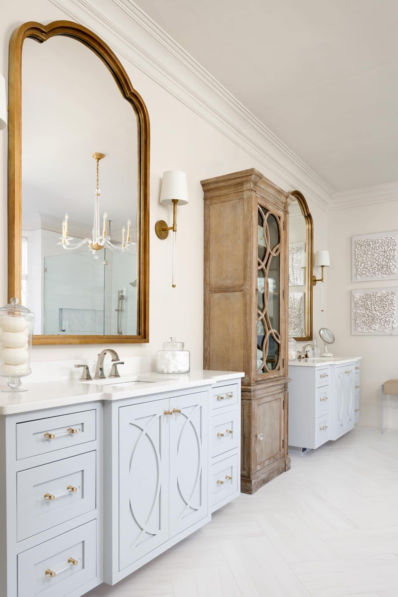 Elegant bathroom with light blue vanity, gold framed mirror, and wooden cabinet.