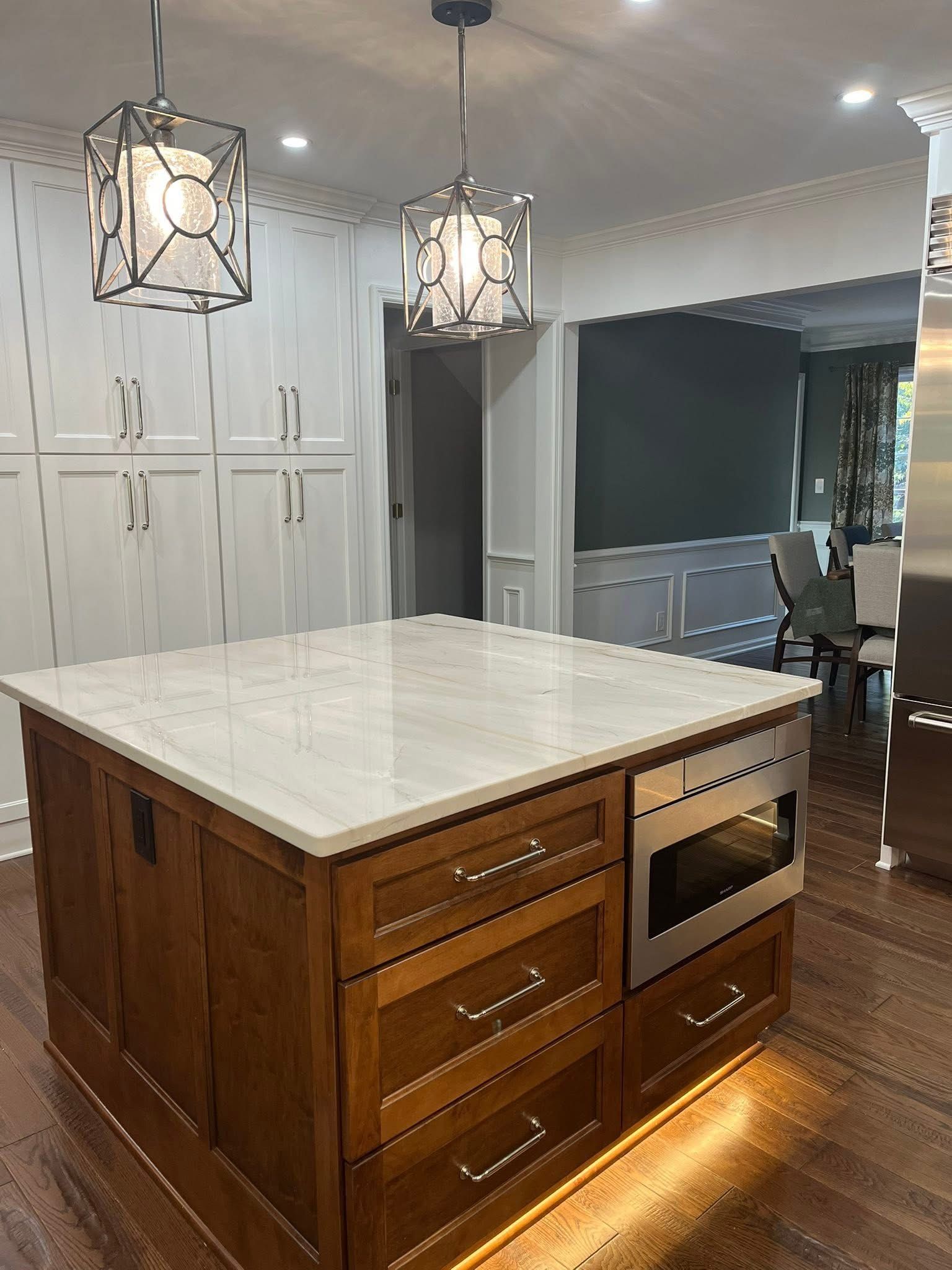 Kitchen with a wooden island, white countertops, built-in microwave, and pendant lights.