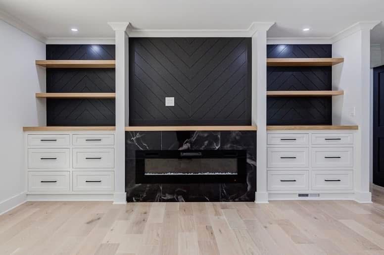 Built-in entertainment center with fireplace. Black tile and marble surround, white cabinets, light wood shelves, and floors.