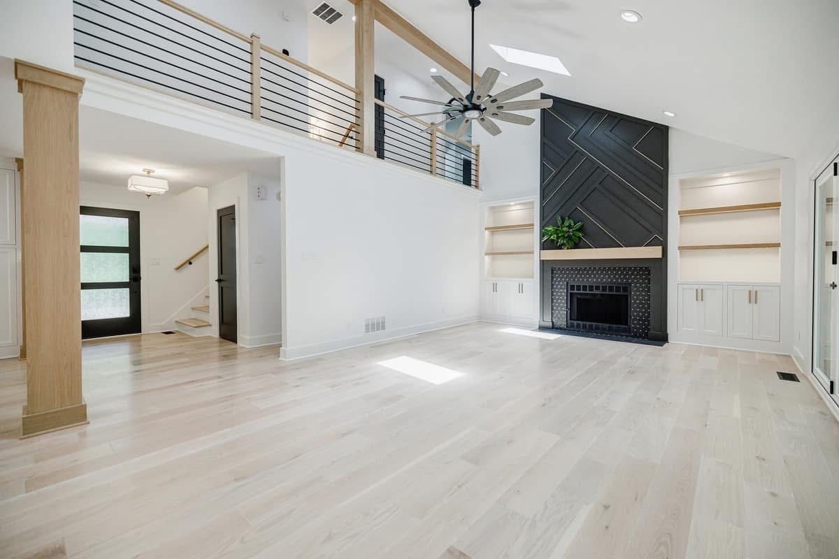 Spacious, bright living room with white walls, light wood floors, fireplace, and balcony.