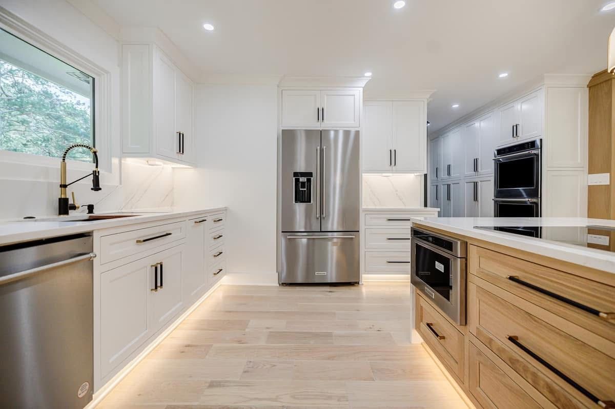 Modern white and wood kitchen with stainless steel appliances, marble countertops, and light wood flooring.