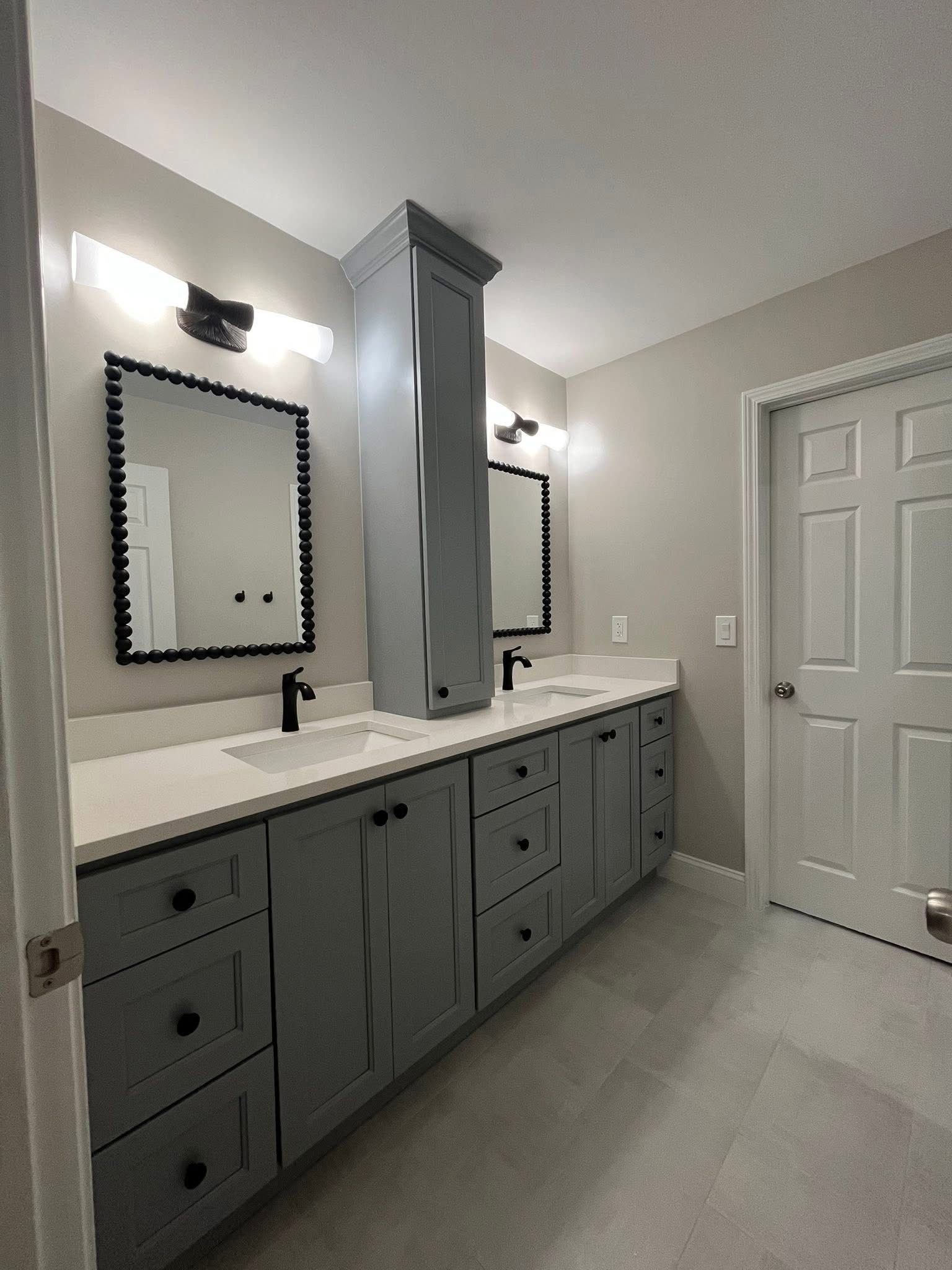 Gray bathroom with double vanity, mirrors, and tall cabinet. White countertop and light fixtures.