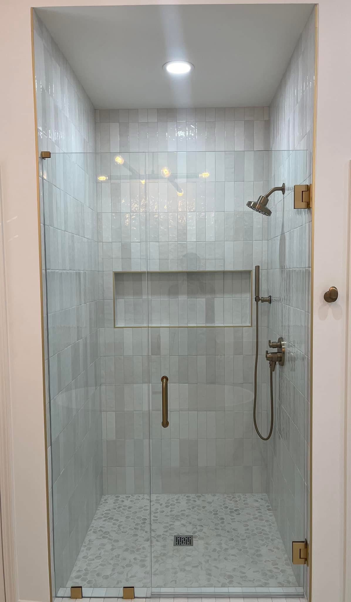 Glass-enclosed shower with white tiled walls, pebble floor, and bronze hardware.