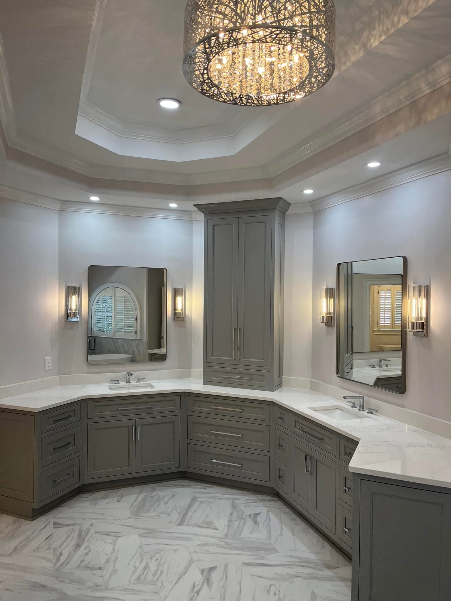 Gray bathroom with a large vanity, tall cabinet, marble floors, and decorative chandelier.