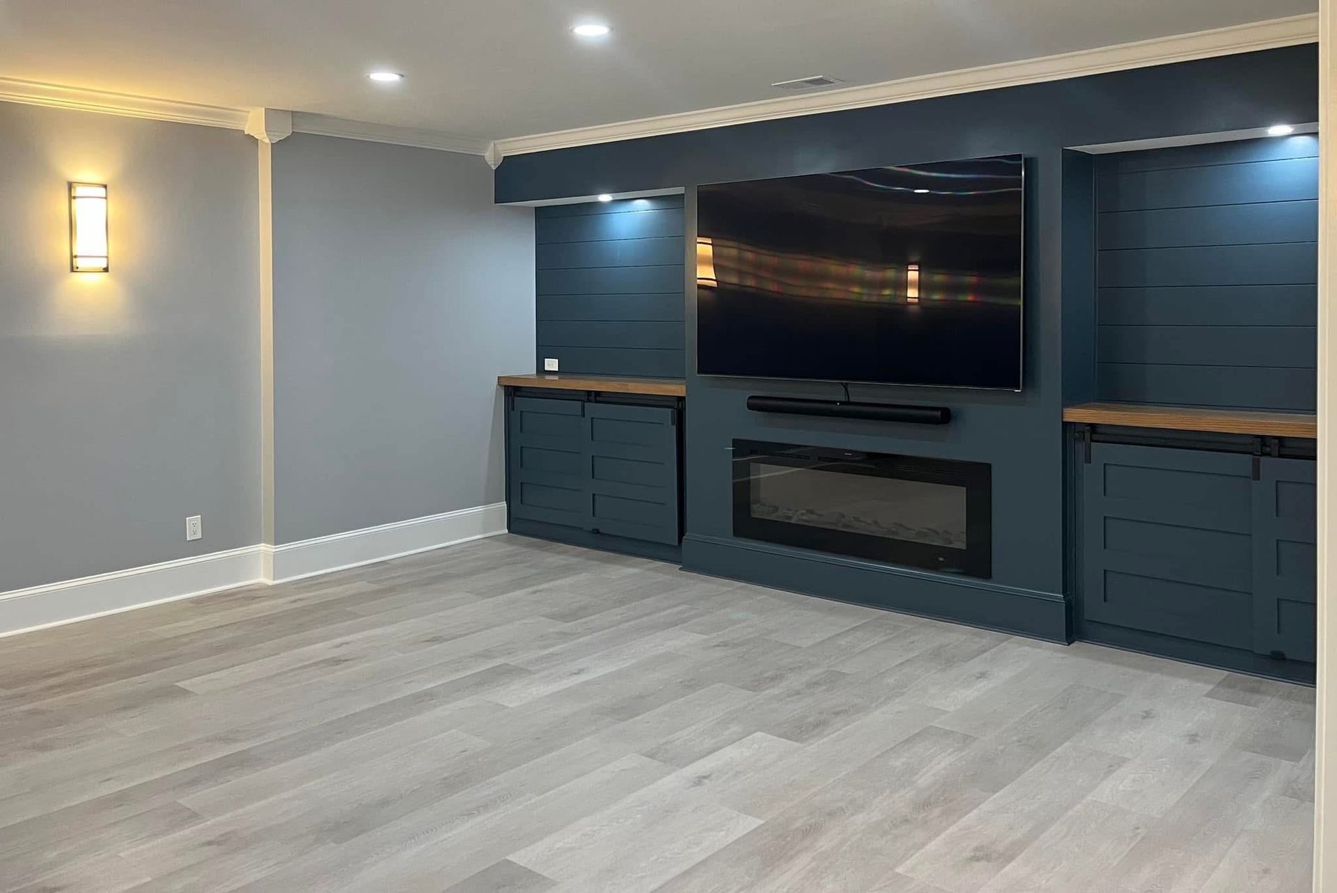 Empty living room with wood flooring, blue accent wall, and built-ins; a TV is mounted above a fireplace.