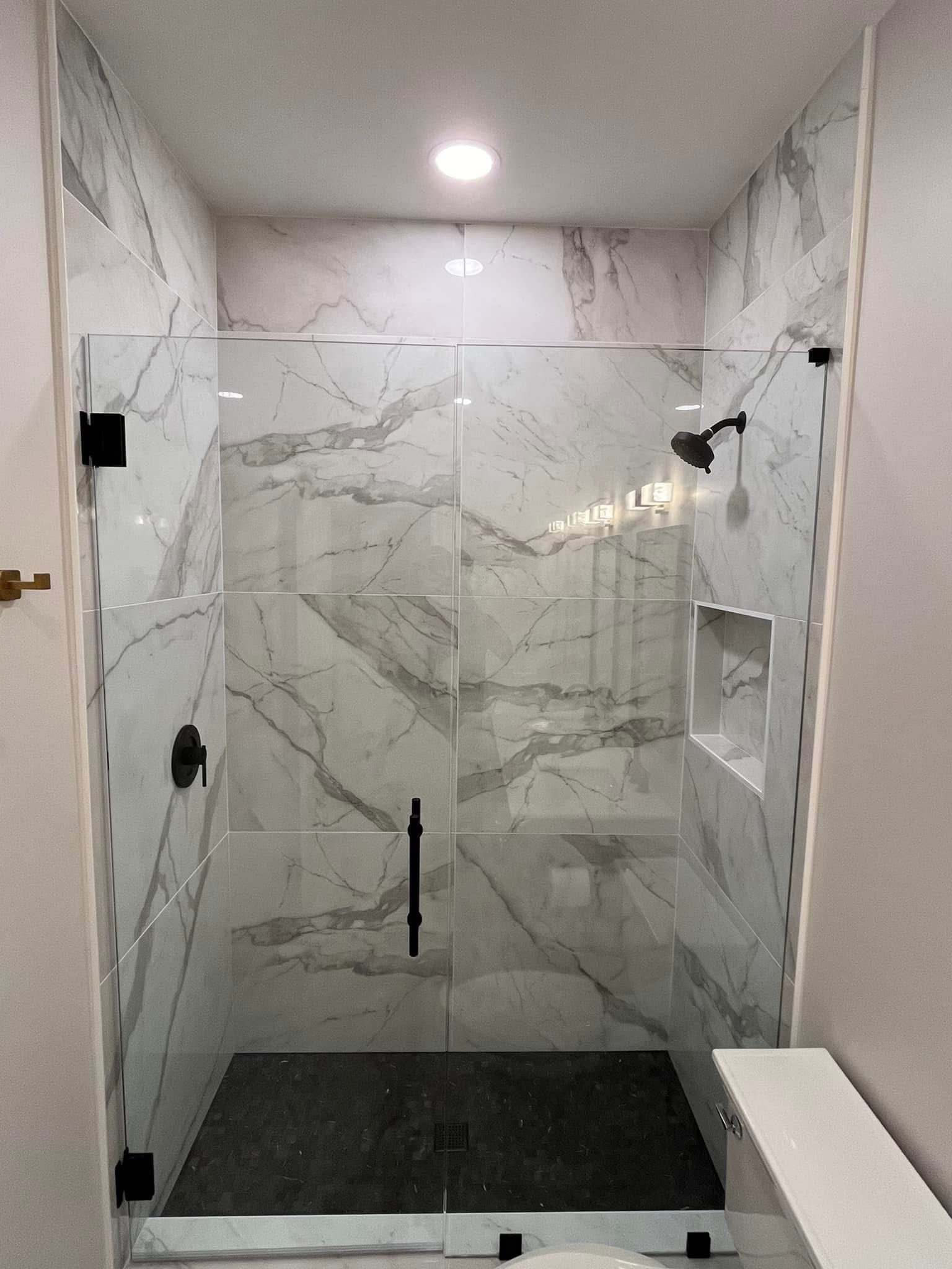 Marble-tiled shower with black hardware, glass door, and a built-in shelf.
