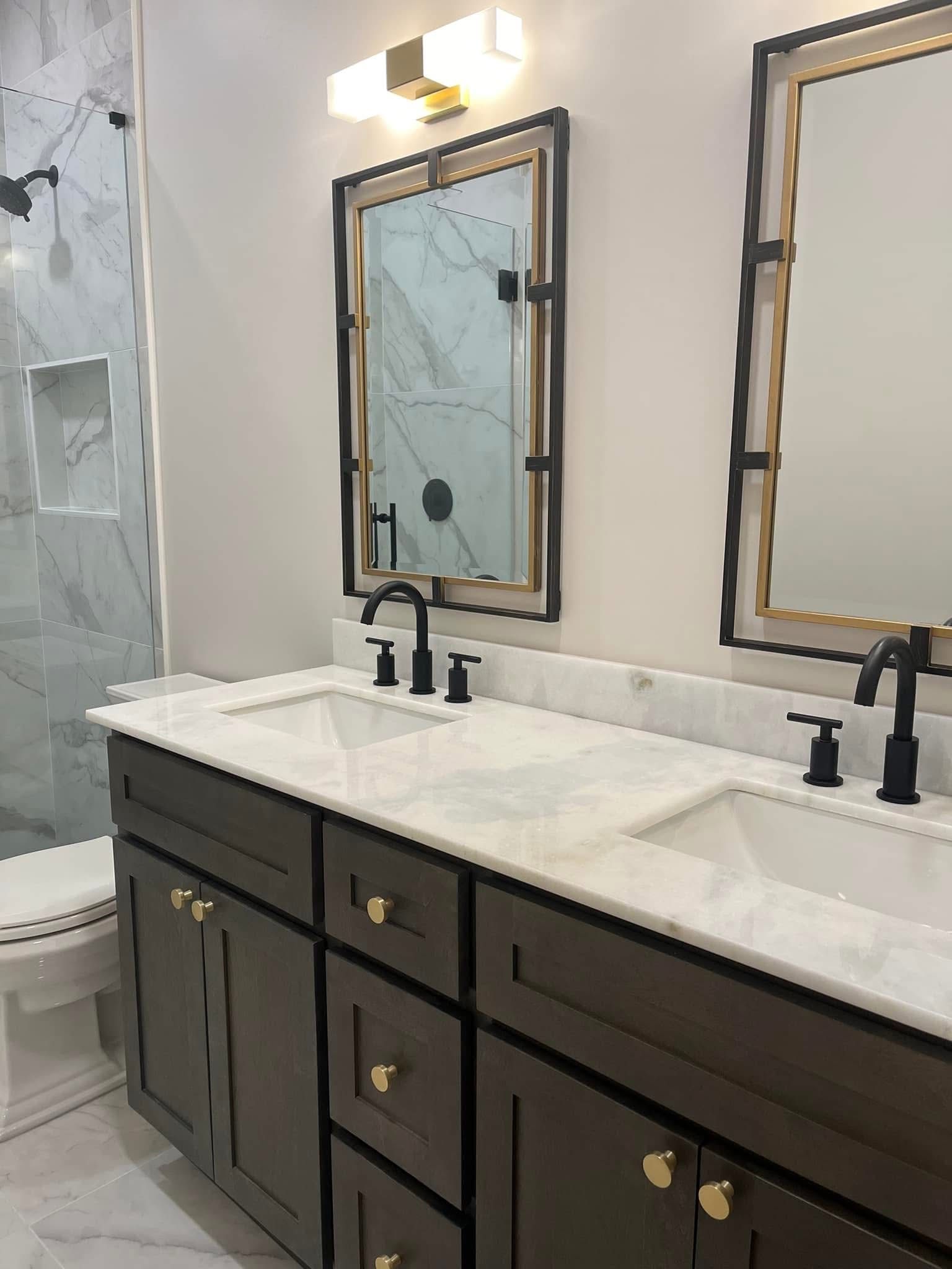Bathroom with double vanity, marble countertop, black fixtures, and gold-framed mirrors.