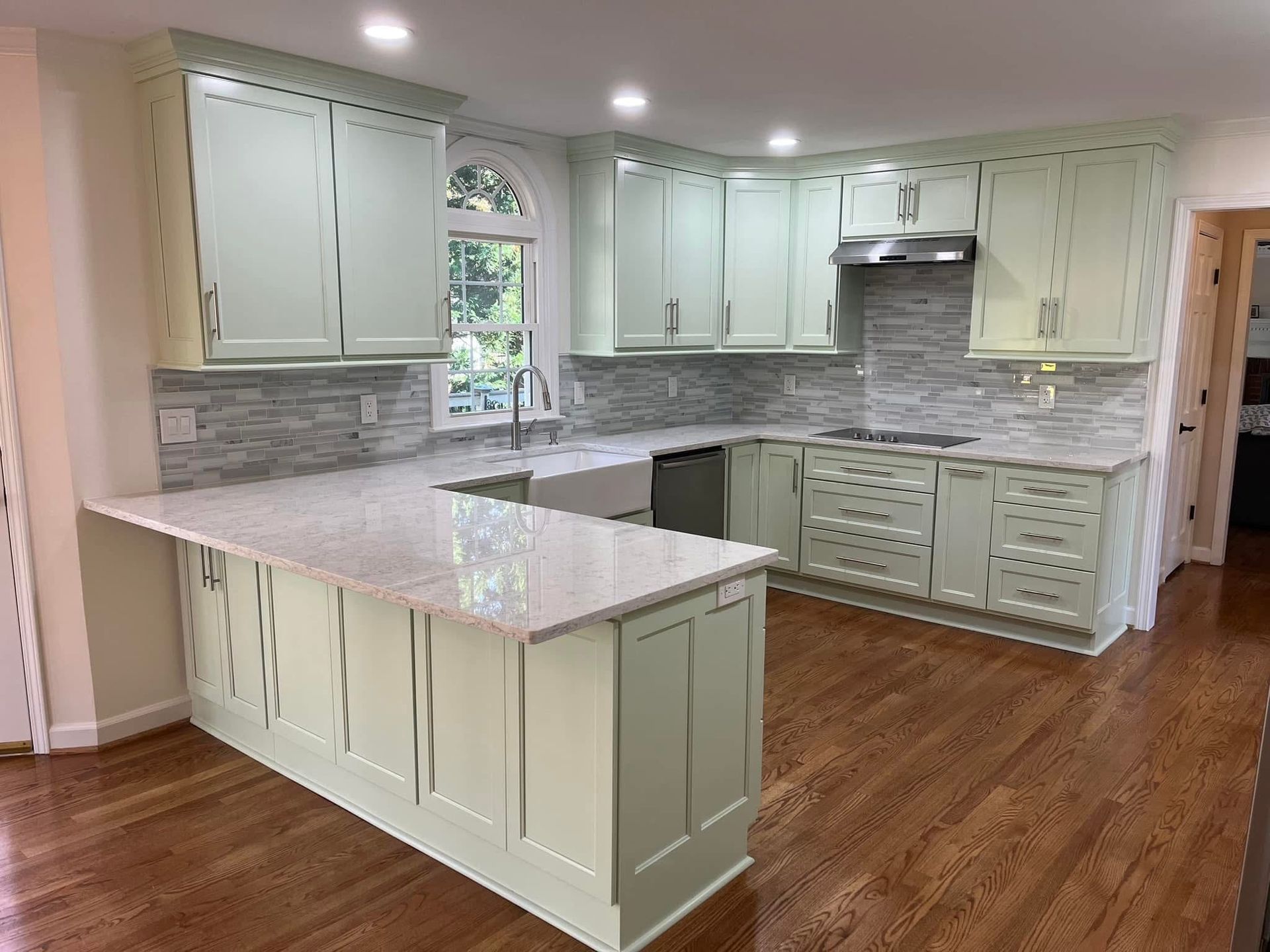 Green kitchen with light countertops and wood flooring.