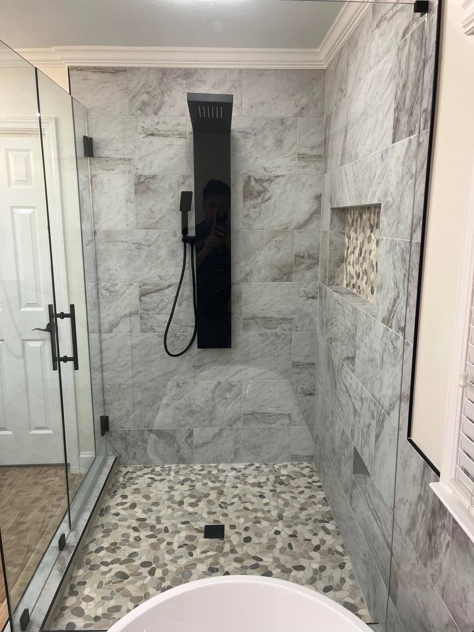 Modern shower with stone tile walls, pebble floor, glass door, and black showerhead fixture.