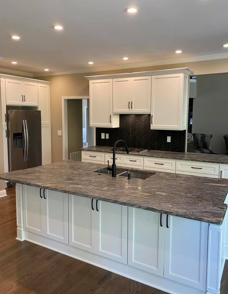 White kitchen with island and dark countertops, cabinets with black hardware, stainless steel fridge.