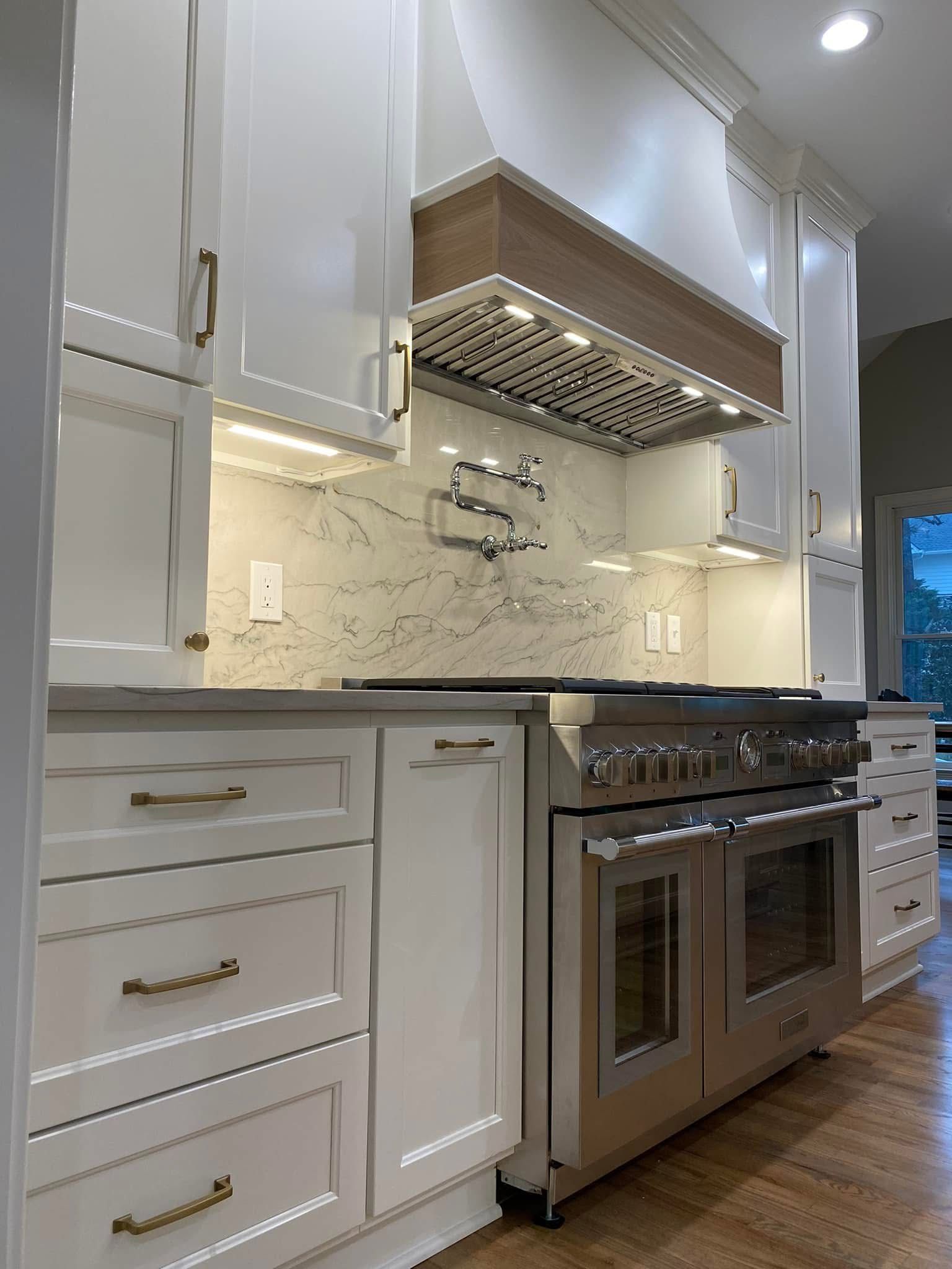 White kitchen with stainless steel oven, cabinets, and a wooden range hood.