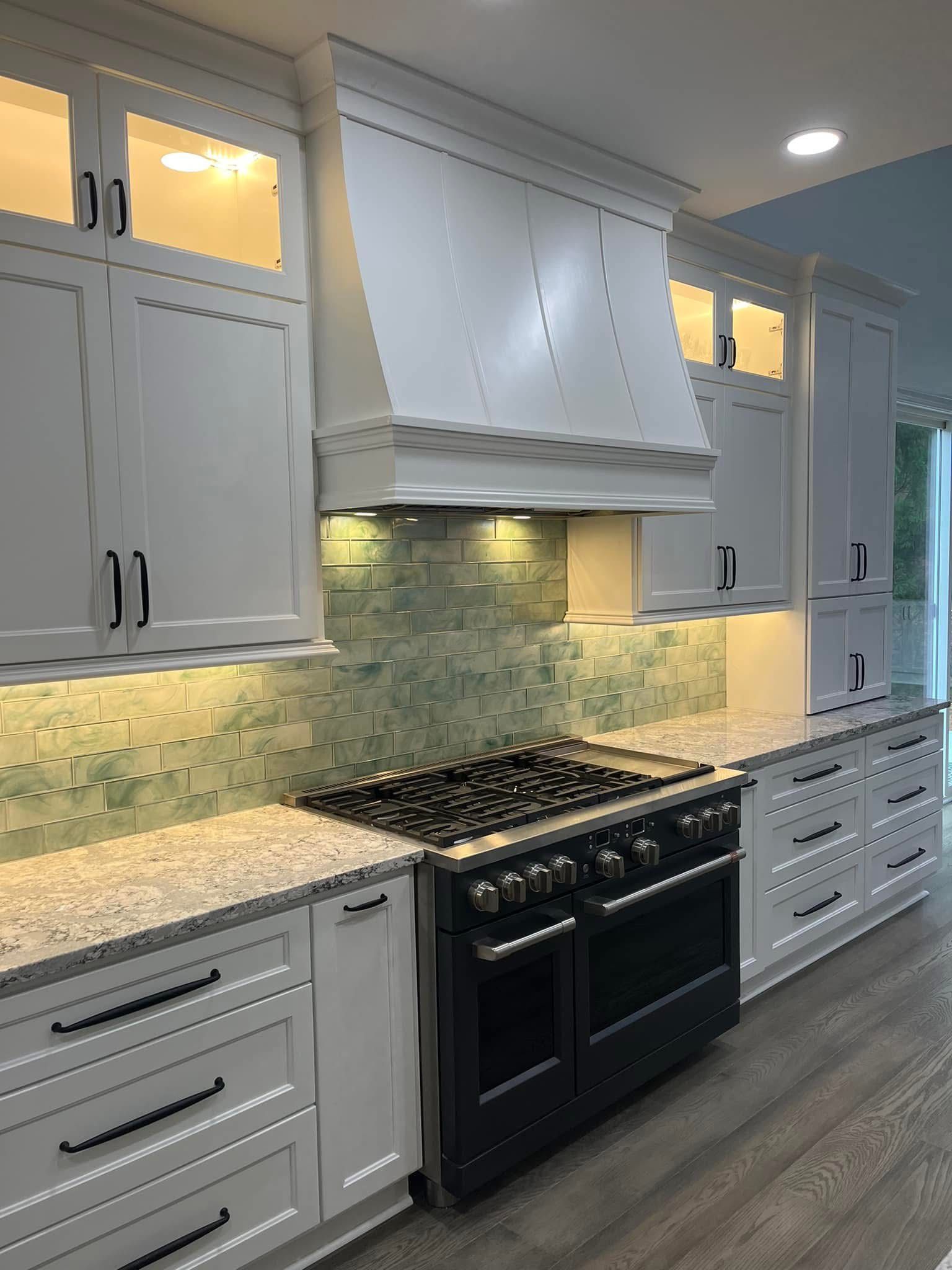 White kitchen with a black stove, range hood, and light-colored backsplash.