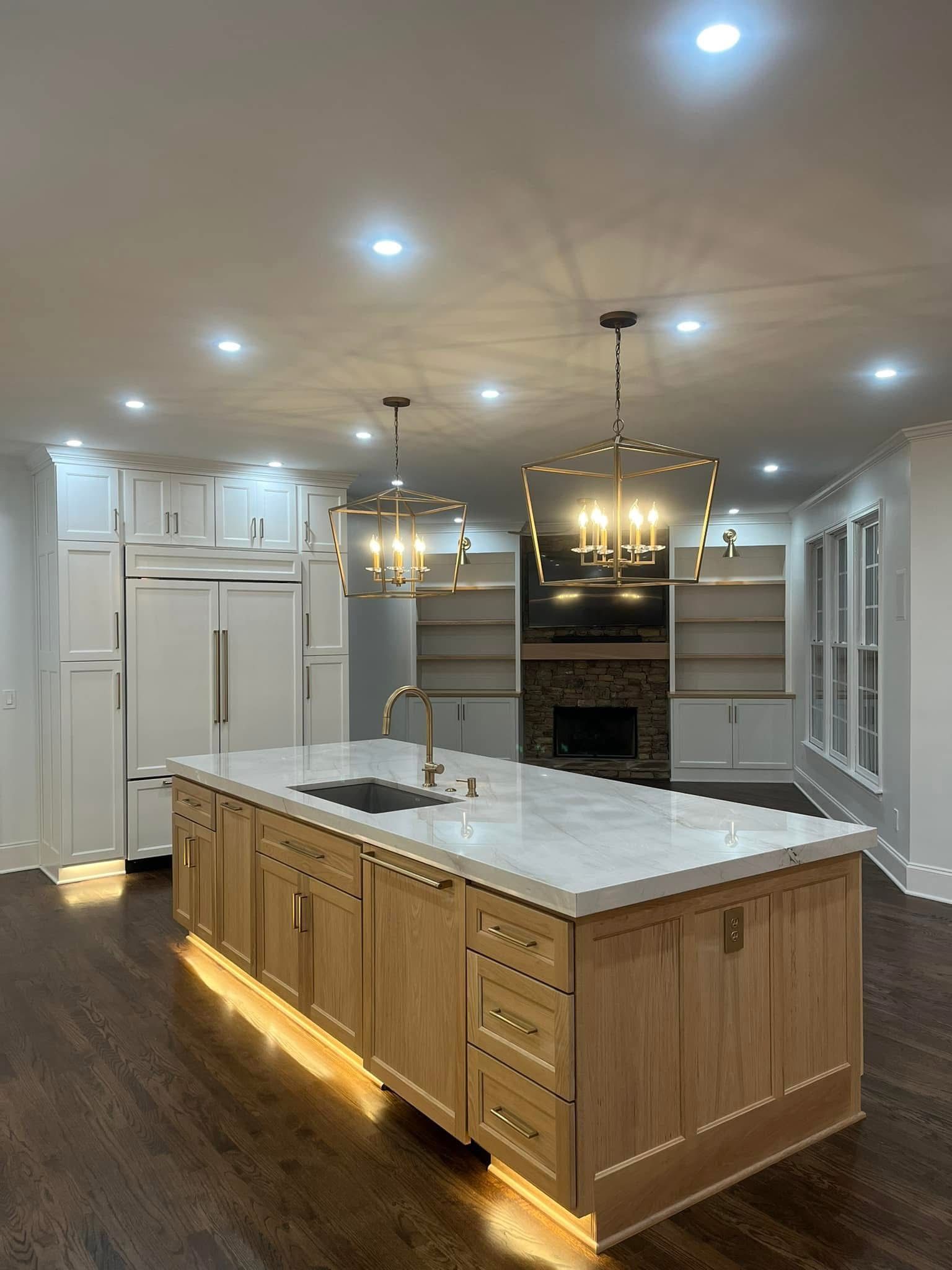 Modern kitchen with large island, light wood cabinets, marble countertop, and gold light fixtures.