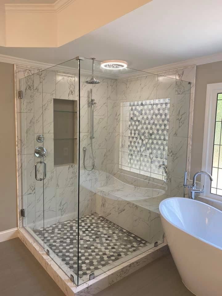 Corner shower with glass doors, marble tile, built-in bench, and patterned floor tile.