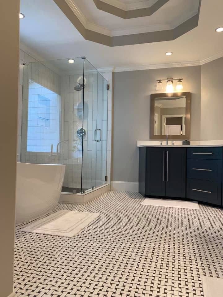 Bathroom with a freestanding tub, glass shower, dark blue vanity, and black and white patterned floor tiles.