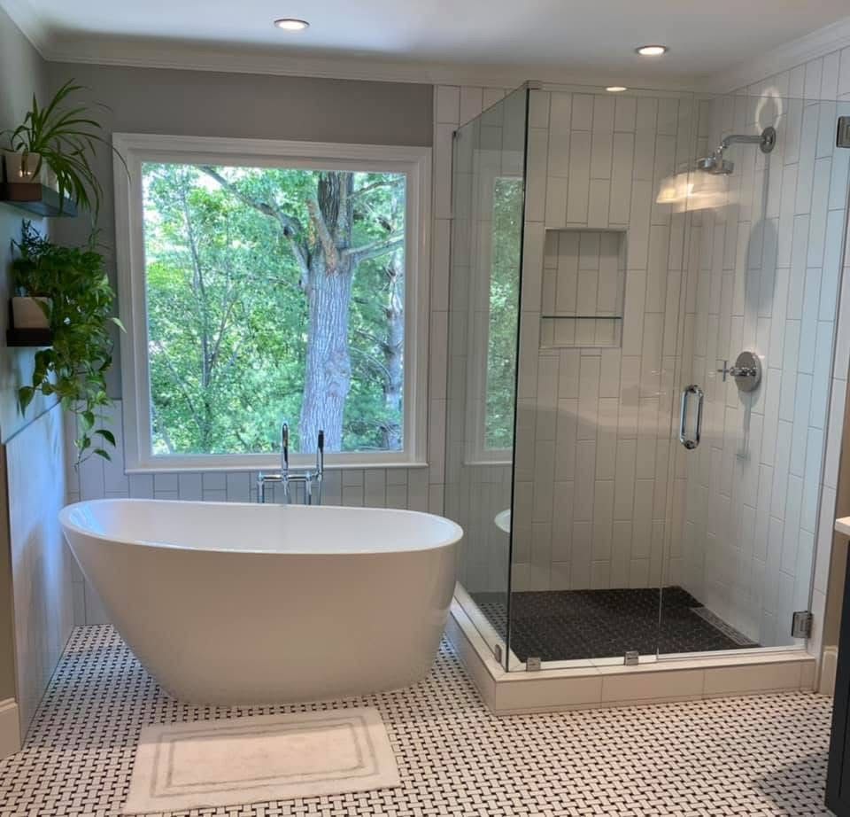 Modern bathroom with freestanding tub, glass shower, and window overlooking trees. White, gray, and black colors.