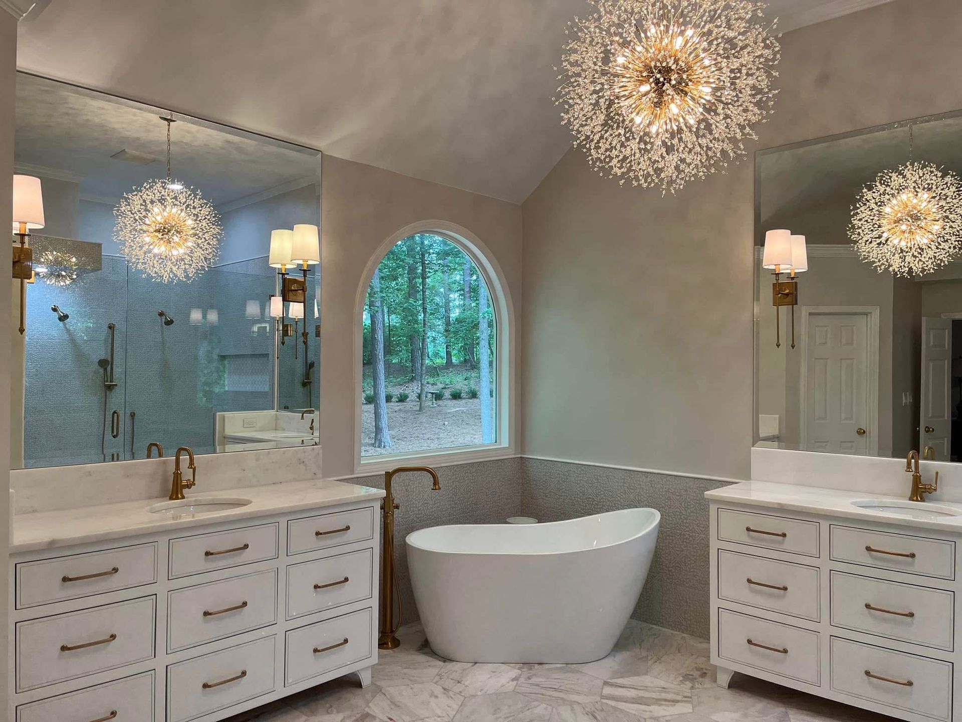 Luxurious bathroom with white cabinetry, freestanding tub, and sparkling chandelier.