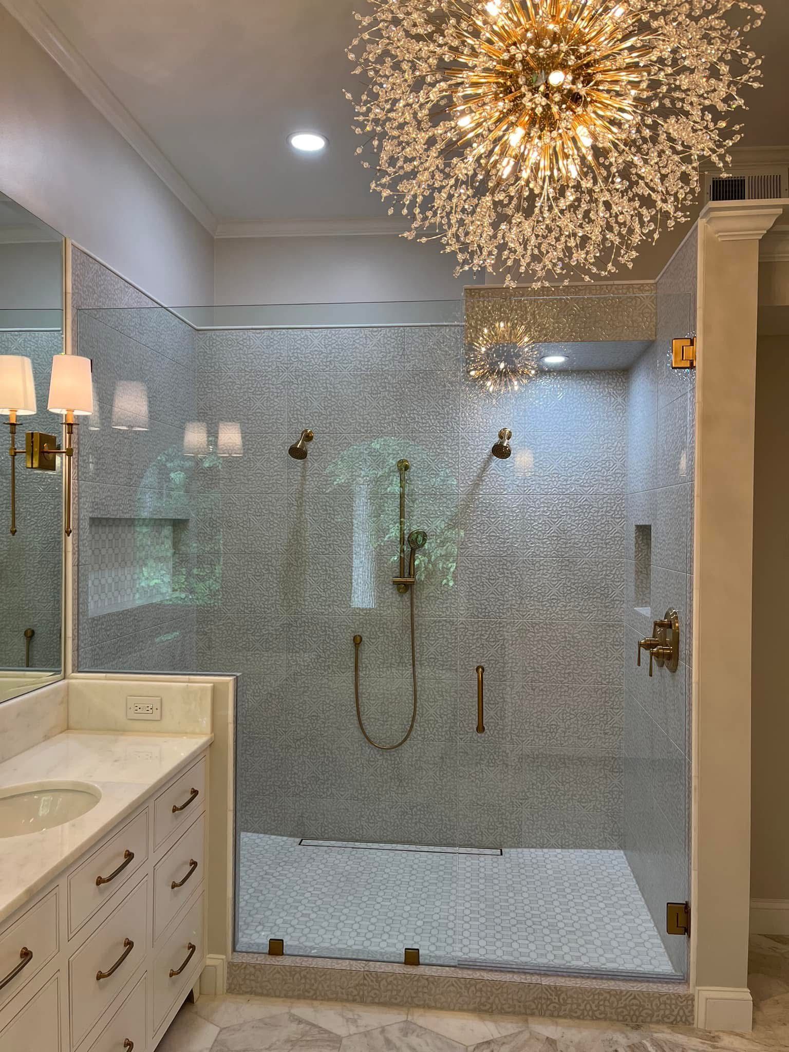 Bathroom with glass shower, mosaic tile walls, and brass fixtures.  A chandelier hangs overhead.