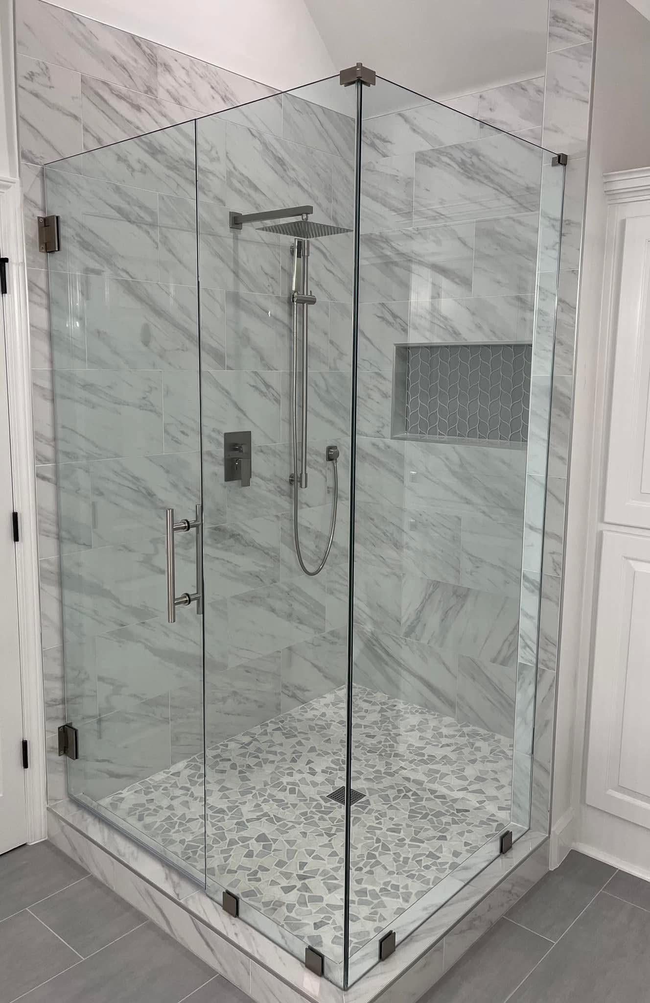 Glass shower enclosure with gray and white tile, showerhead, and a mosaic tile floor.