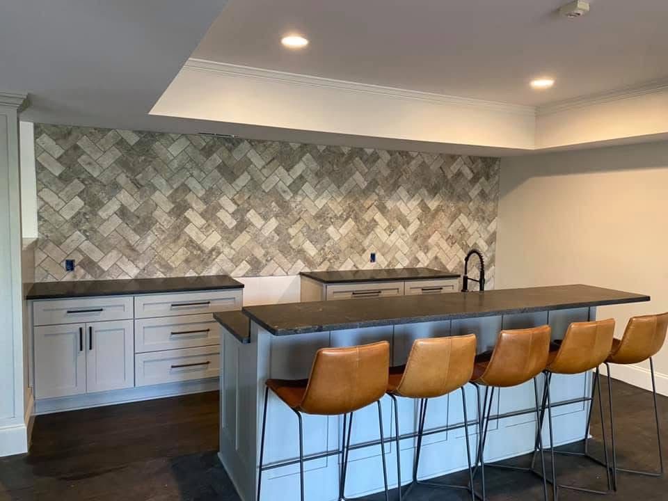 Modern kitchen with a light gray and herringbone tile backsplash, gray countertops, and bar seating with brown leather stools.