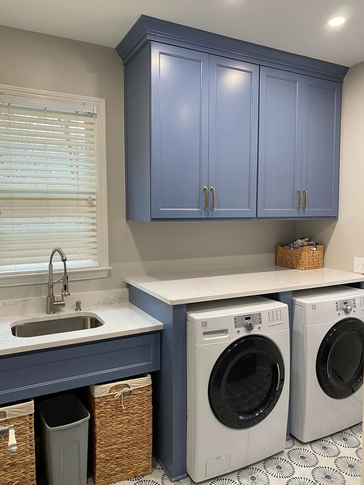 Laundry room with blue cabinets, white countertops, and washer/dryer.