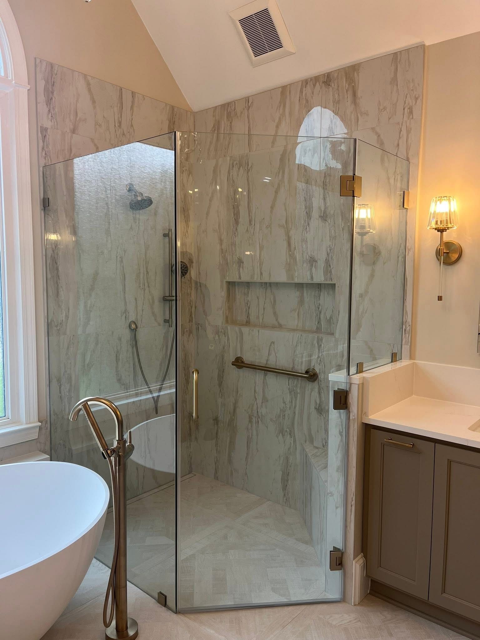 A modern bathroom with a glass shower enclosure, marble-like walls, and a freestanding tub.