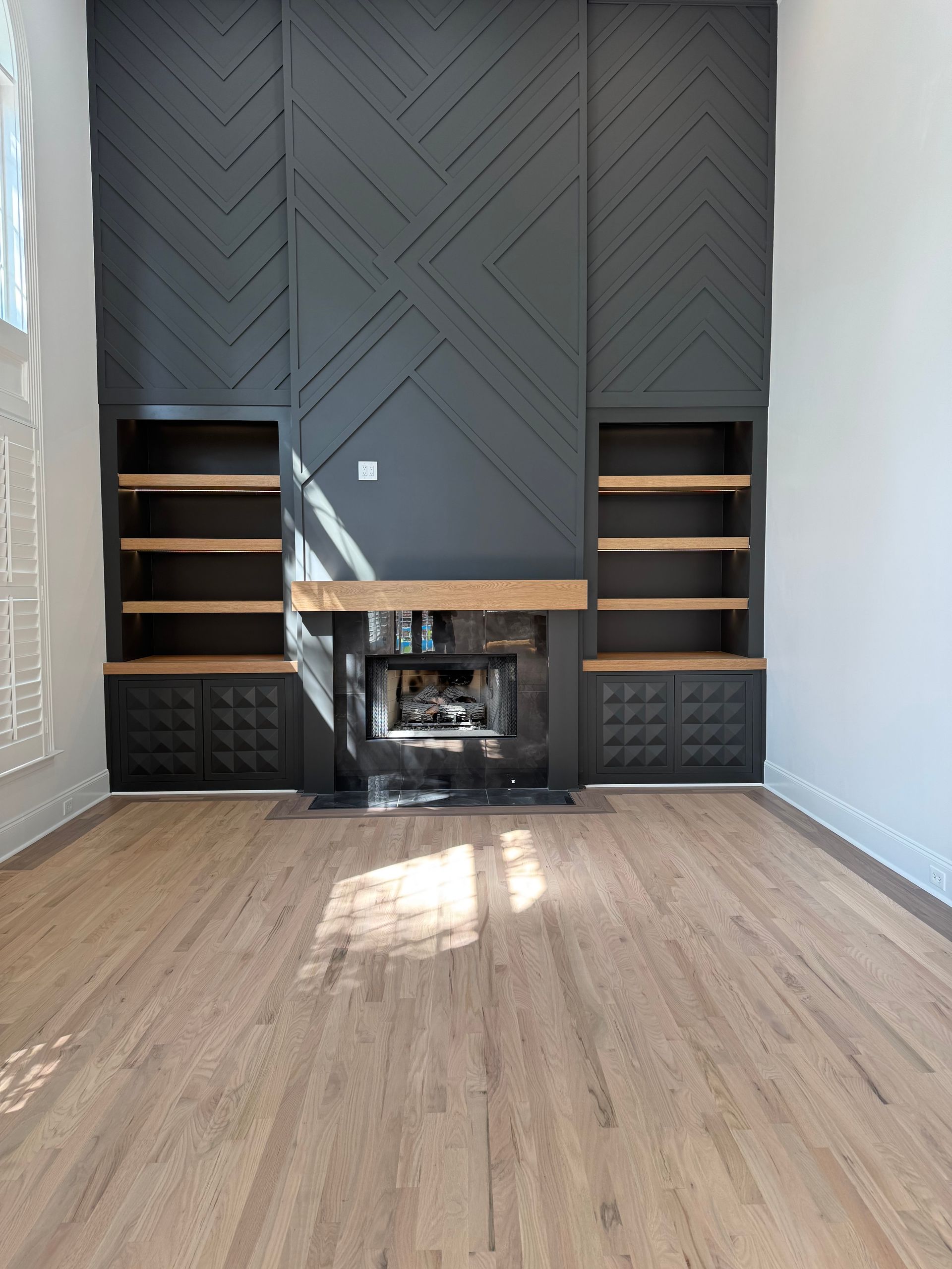 Living room with dark gray herringbone wall paneling, built-in bookshelves, fireplace, and hardwood floors.