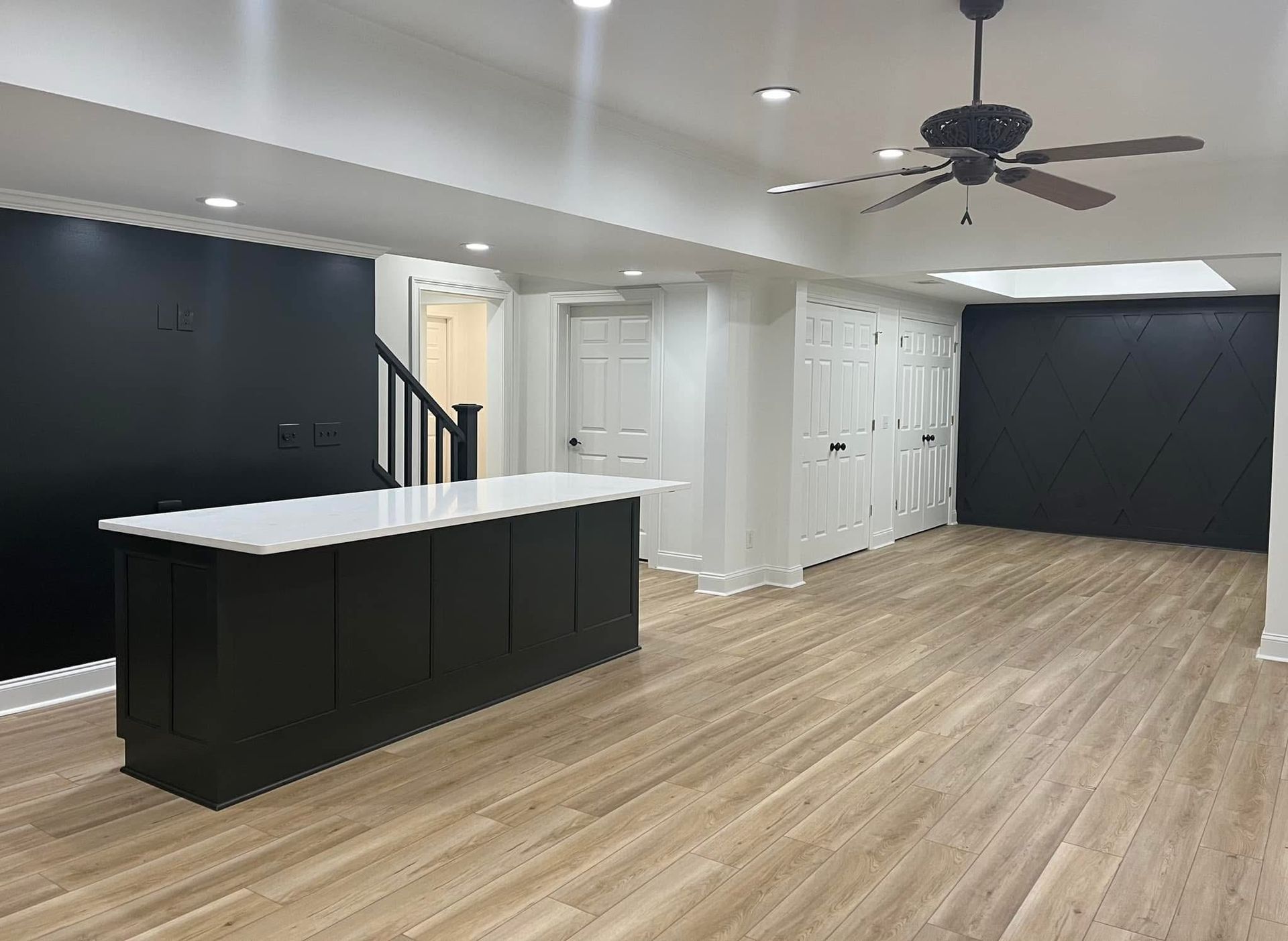 Modern kitchen with black island, white countertop, dark accent walls, and wood-look flooring.
