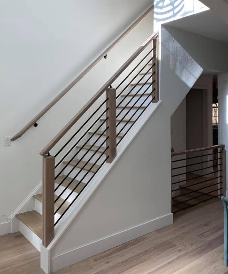 Staircase with light wood handrails, black metal rods, and white walls, in a modern interior setting.