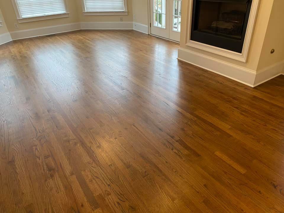 Polished hardwood floors in a room, reflecting light. Fireplace and windows visible.