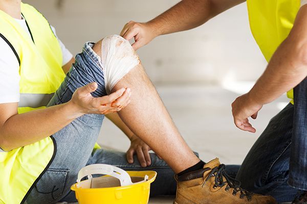 A construction worker is sitting on the floor with a bandage on his knee.