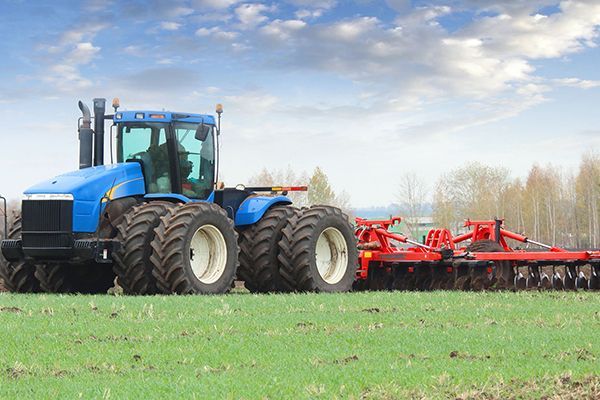 A blue tractor is plowing a field with a red plow attached to it.