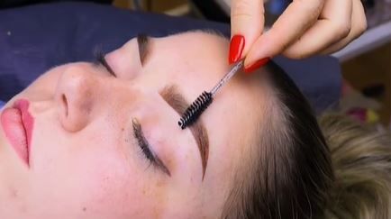 A woman is getting her eyebrows brushed by a makeup artist