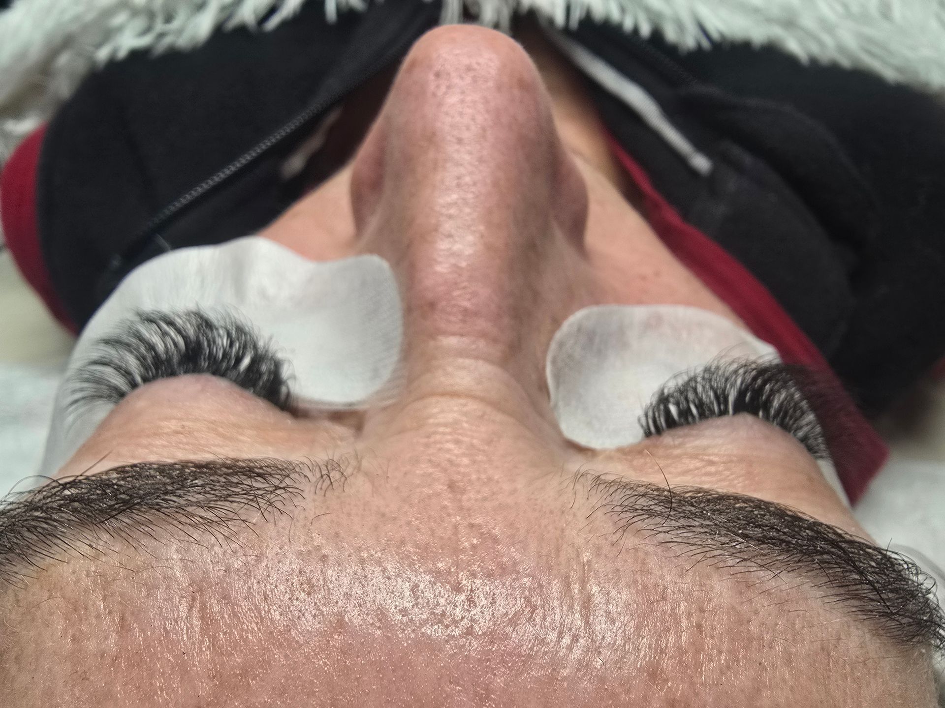 A woman with prominent long eyelashes, displaying a set of false eyelashes beside her for visual contrast.