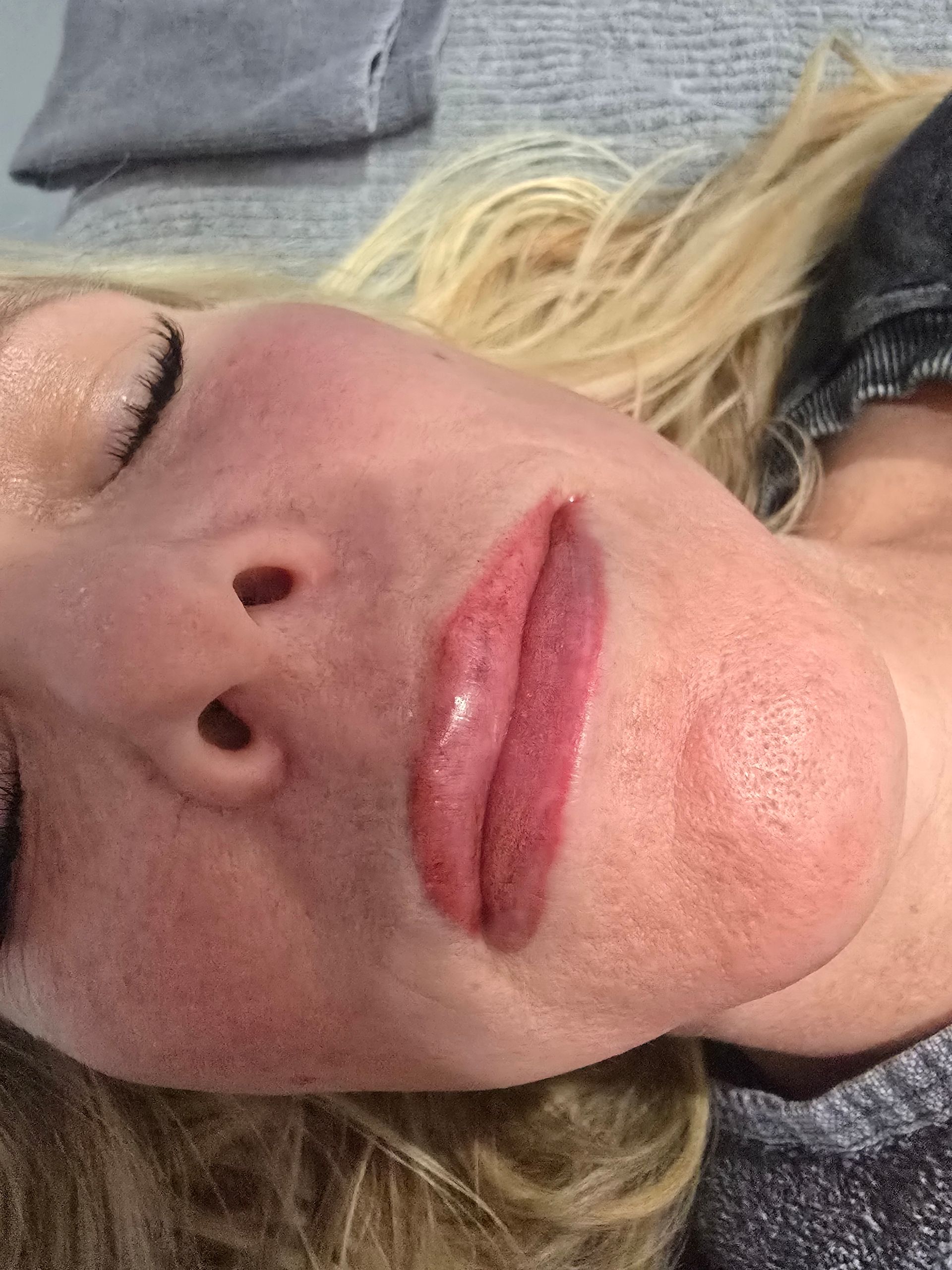 A woman is laying down with her eyes closed and her lips painted.