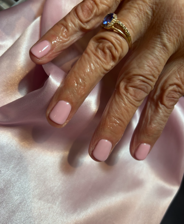 A woman 's hand with pink nails and a gold ring.