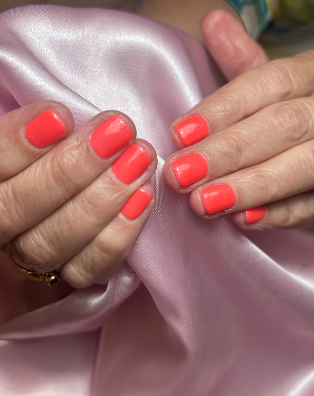 A close up of a woman 's hands with bright orange nails.