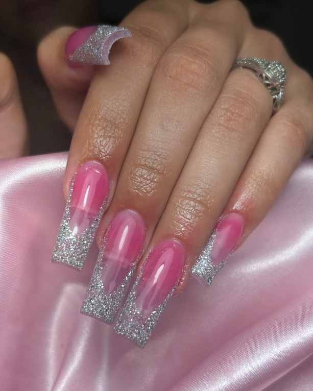 A woman 's hand with pink and silver nails and a ring.