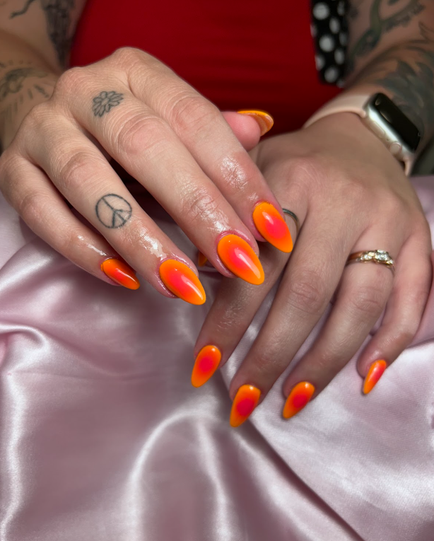 A woman 's hands with bright orange nails and a peace sign tattoo.