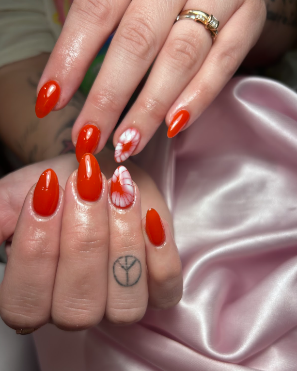 A woman 's hand with red nails and a peace sign tattoo on her ring finger.