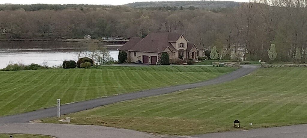 A house is sitting on top of a lush green field next to a lake.