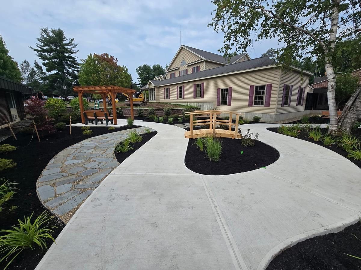 A concrete walkway leading to a house with a wooden bridge