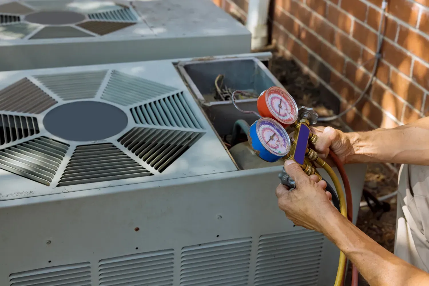 Technician checking HVAC unit with pressure gauges beside a brick wall