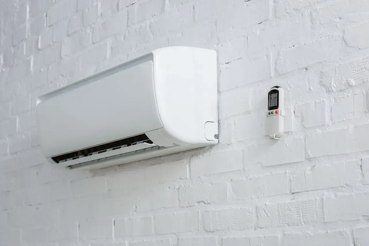 White wall-mounted air conditioner on a white brick wall beside a small thermostat.